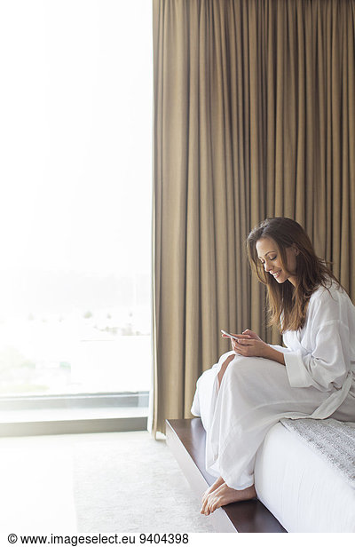 Smiling woman in bathrobe texting in bedroom