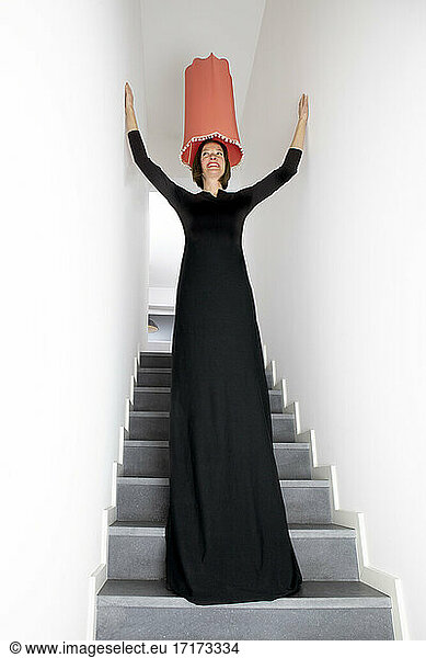 Smiling woman in black dress with arms raised standing on staircase