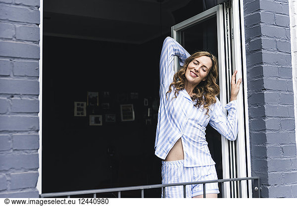 Smiling woman in pyjama at home stretching at the balcony