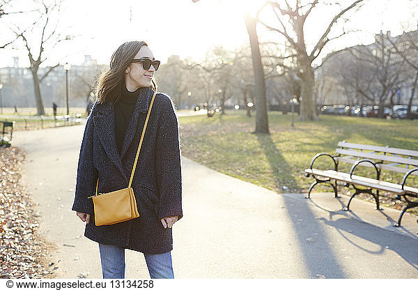 Smiling woman in sunglasses standing on footpath during sunny day
