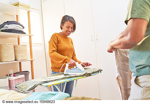 Smiling woman ironing pants at home