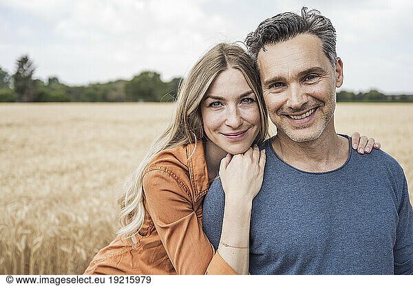 Smiling woman leaning on mature man in field