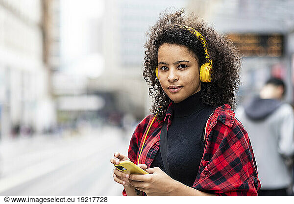 Smiling woman listening to music through headphones in city