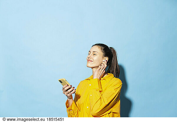 Smiling woman listening to music through wireless earphones against blue background