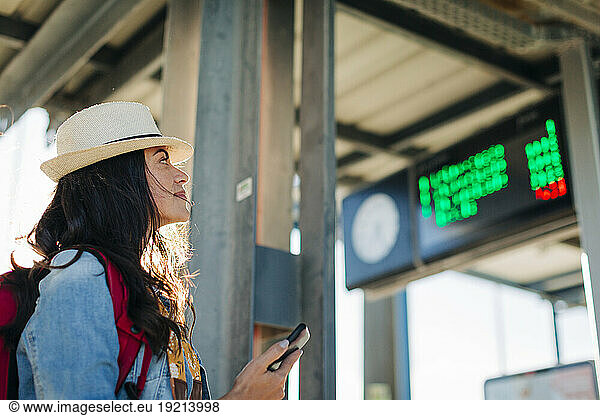 Smiling woman looking at arrival departure board at tram station