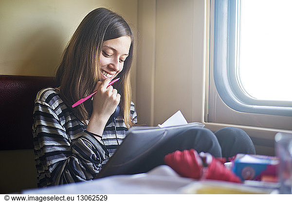 Smiling woman looking at book while travelling in train