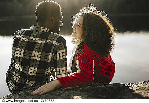 Smiling woman looking at boyfriend while relaxing by lake