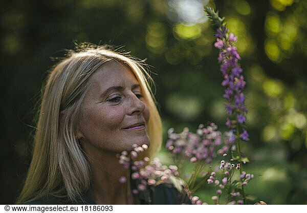 Smiling woman looking at flowering plant in garden