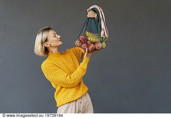 Smiling woman looking at mesh bags with fruits against black background