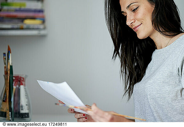 Smiling woman looking at paper at home