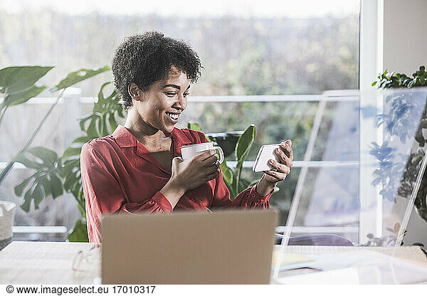 Smiling woman looking at smart phone at desk at home