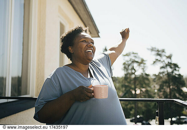 Smiling woman looking away while holding coffee cup in balcony