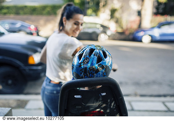 Smiling woman looking son sitting on bicycle by street