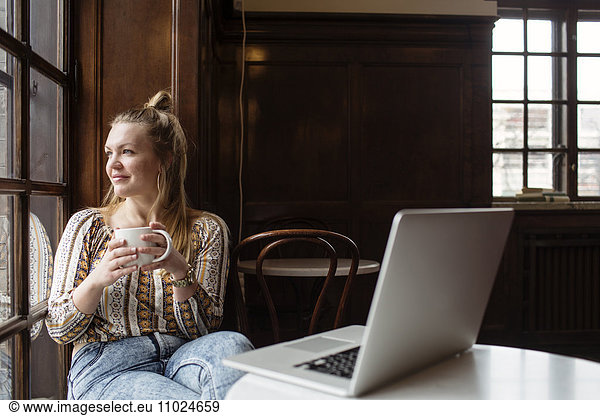 Smiling woman looking through window while sitting at cafe