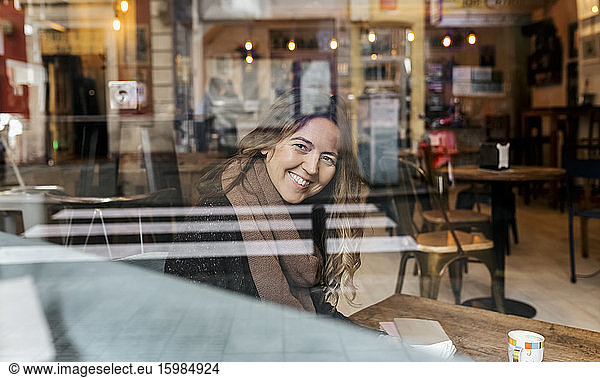 Smiling woman looking through windowpane in coffee shop