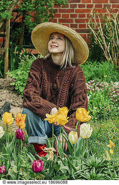 Smiling woman looking up crouching near tulips in garden