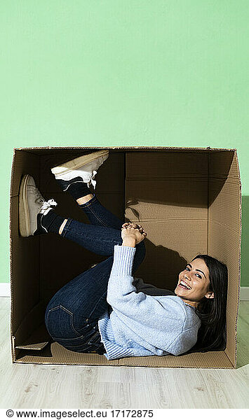 Smiling woman lying in cardboard against green background