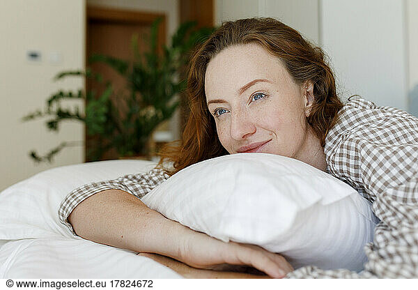 Smiling woman lying on bed with pillow in bedroom