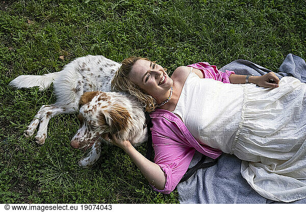 Smiling woman lying with dog in park