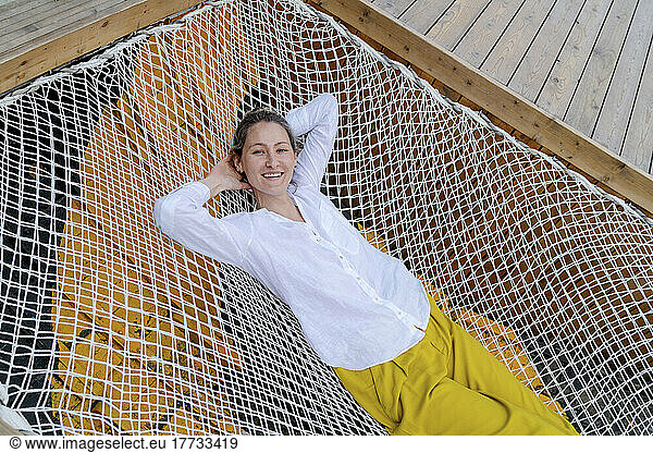 Smiling woman lying with hands behind head on hammock