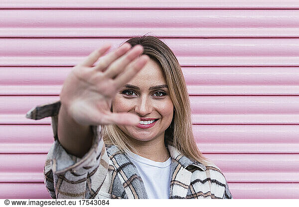 Smiling woman making hand sign in front of pink shutter