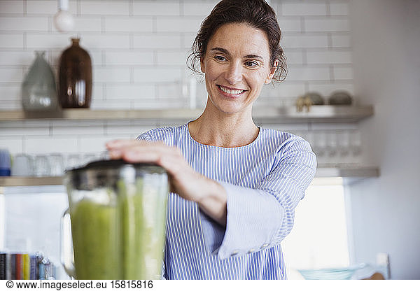 Smiling woman making healthy green smoothie in kitchen