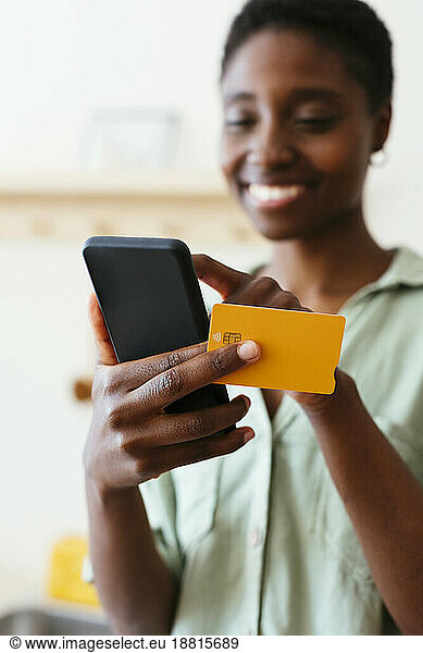 Smiling woman making payment through credit card on mobile phone at home