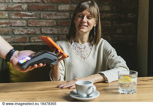 Smiling woman making payment through smart phone at cafe