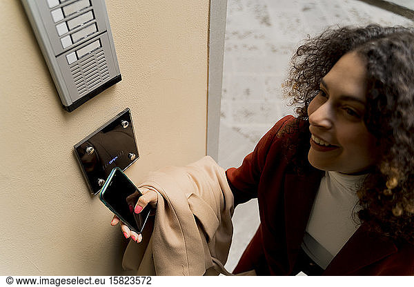 Smiling woman opening door with smartphone