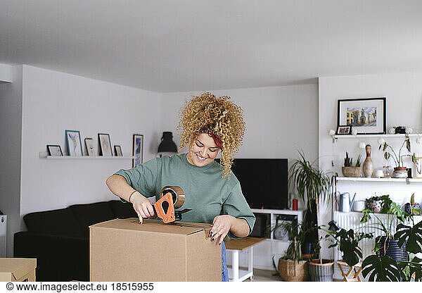 Smiling woman packing box with adhesive tape