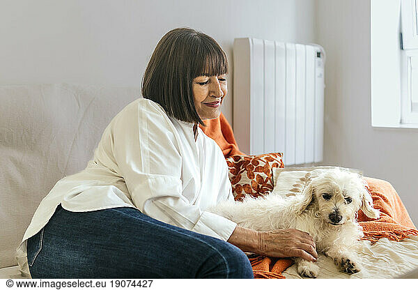 Smiling woman petting dog on bed at home