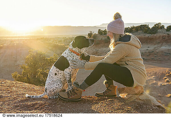 Smiling woman petting dog while sitting at desert on sunny day