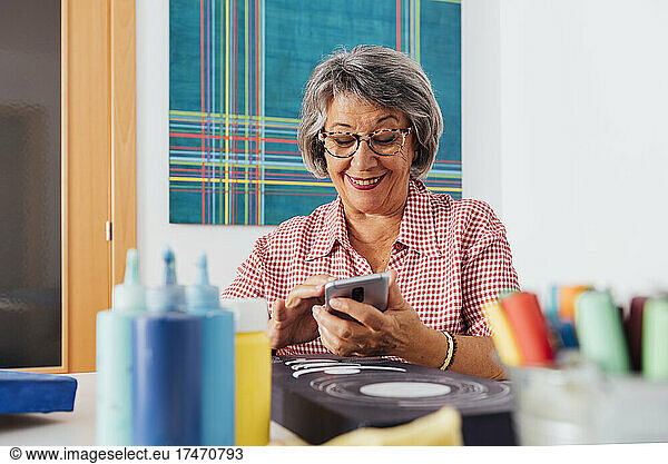 Smiling woman photographing painting through smart phone at home
