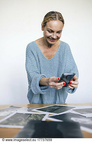 Smiling woman photographing photos through smart phone