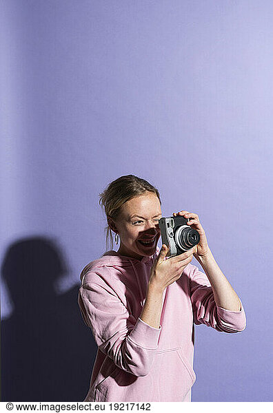 Smiling woman photographing through camera in studio