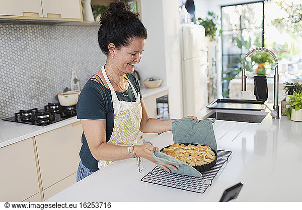 Smiling woman placing hot homemade apple pie on cooling rack