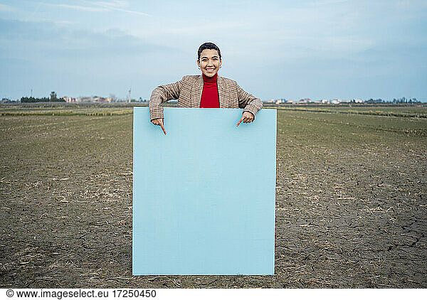 Smiling woman pointing at blue painting on field