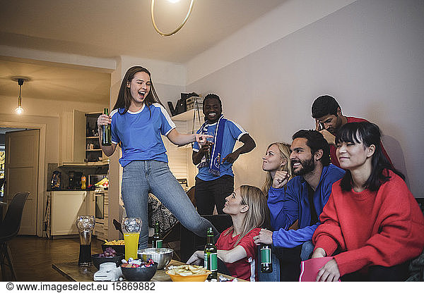 Smiling woman pointing at female while watching sport with friends at home