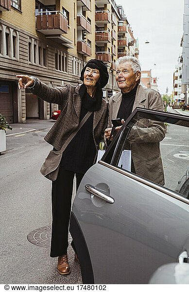 Smiling woman pointing while senior man holding smart phone by car on street