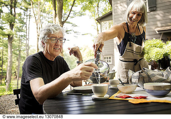 Smiling woman pouring coffee to senior man at table in yard