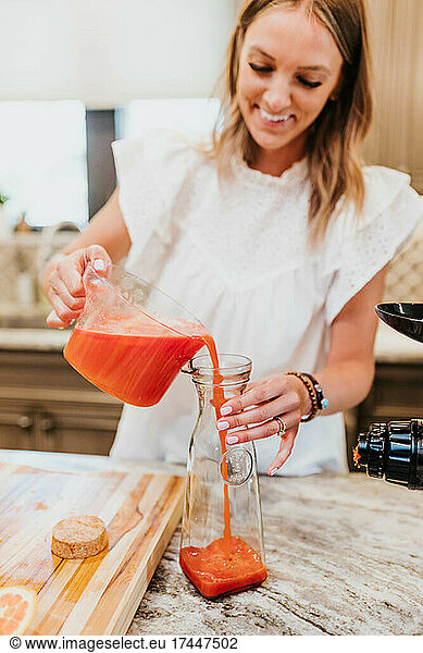 Smiling woman pours freshly juiced fruits and vegetables into carafe