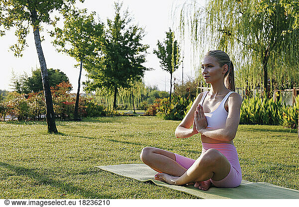 Smiling woman practicing padmasana pose on exercise mat in park