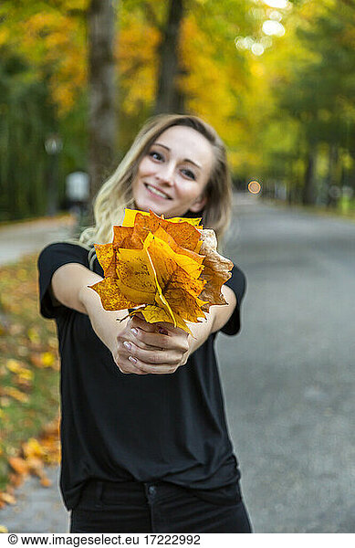 Smiling woman presenting bunch of autumn leaves