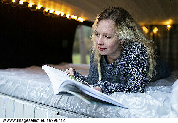Smiling woman reading book while lying on bed in camper van