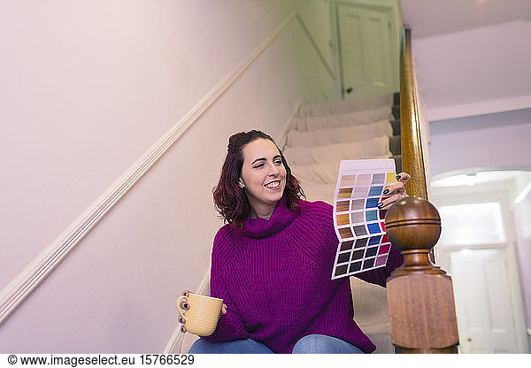 Smiling woman redecorating  looking at paint swatch on stairs