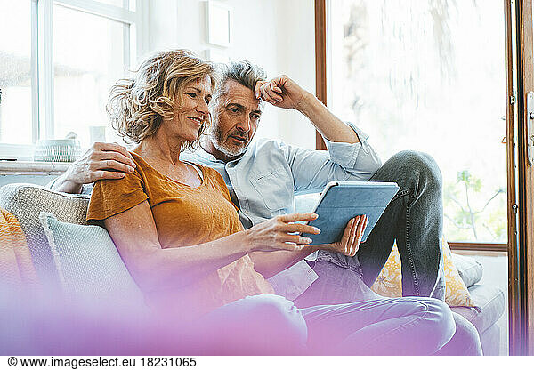 Smiling woman sharing tablet computer with man on sofa at home