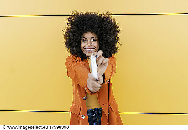 Smiling woman showing testing kit in front of wall