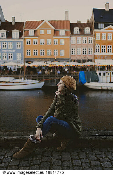 Smiling woman sitting at harbor in front of buildings in city