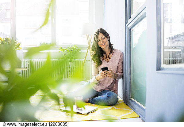 Smiling woman sitting on floor using cell phone