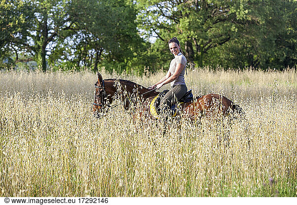 Smiling woman sitting on horseback at agricultural field
